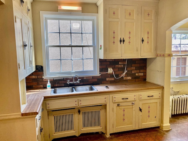 kitchen with a sink, light countertops, arched walkways, radiator heating unit, and decorative backsplash