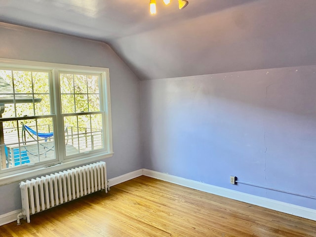 additional living space featuring baseboards, radiator, lofted ceiling, and light wood-style floors