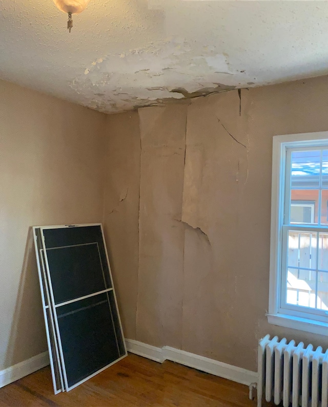 empty room with radiator heating unit, baseboards, and wood finished floors