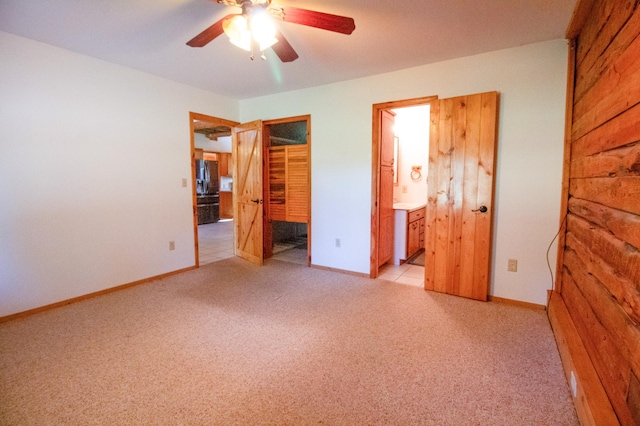 unfurnished bedroom featuring baseboards, ensuite bathroom, ceiling fan, and light colored carpet