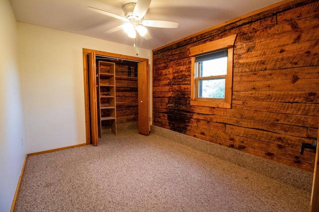 unfurnished bedroom with a closet, baseboards, carpet flooring, ceiling fan, and wood walls