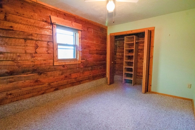 unfurnished bedroom with wooden walls, a closet, ceiling fan, and carpet floors