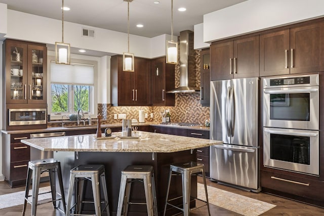 kitchen featuring visible vents, a breakfast bar area, wall chimney range hood, and stainless steel appliances