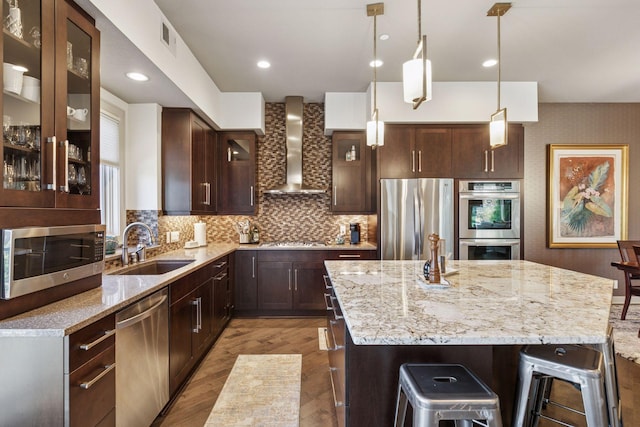 kitchen featuring wood finished floors, a kitchen island, wall chimney exhaust hood, a sink, and stainless steel appliances