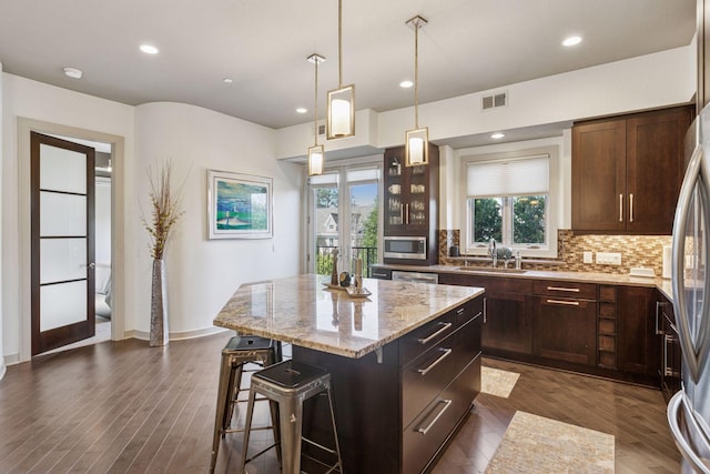 kitchen with light stone countertops, a breakfast bar area, tasteful backsplash, a sink, and appliances with stainless steel finishes