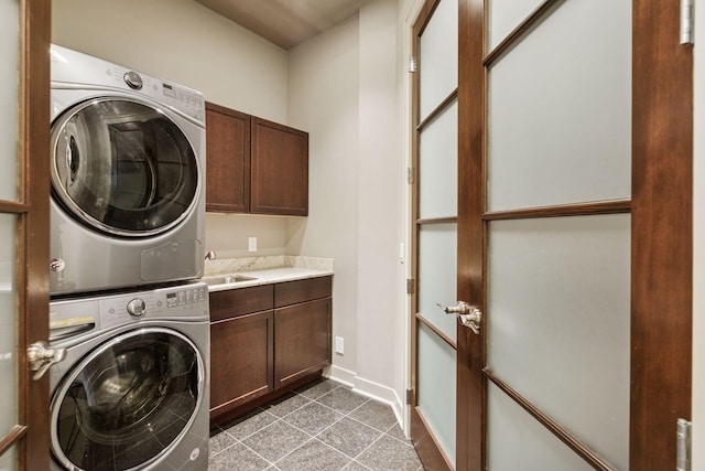 laundry area with stacked washing maching and dryer, baseboards, tile patterned flooring, and cabinet space