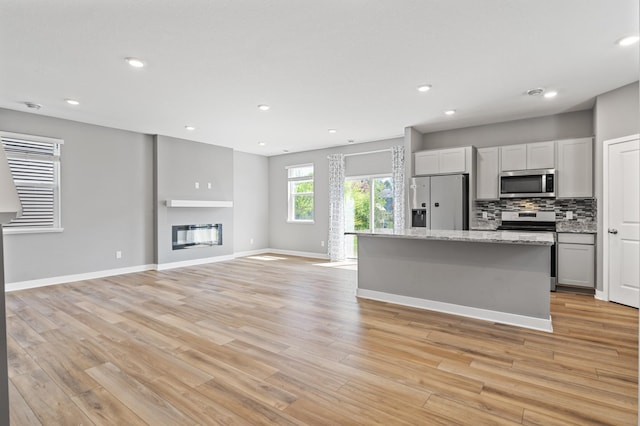 11263 131st Cir N, Dayton, MN 55327 - kitchen featuring appliances with stainless steel finishes, light wood finished floors, a glass covered fireplace, decorative backsplash, and baseboards