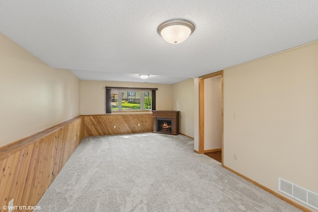 17150 Grenadier Ave, Lakeville, MN 55044 - unfurnished living room featuring a lit fireplace, a textured ceiling, wooden walls, wainscoting, and light carpet
