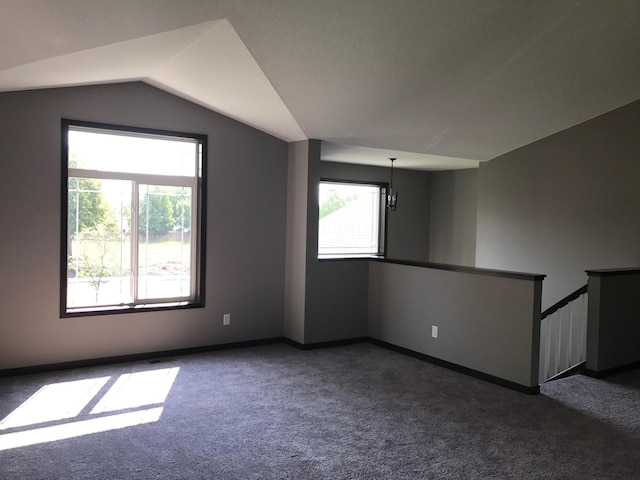 bonus room with a healthy amount of sunlight, vaulted ceiling, dark colored carpet, and a chandelier