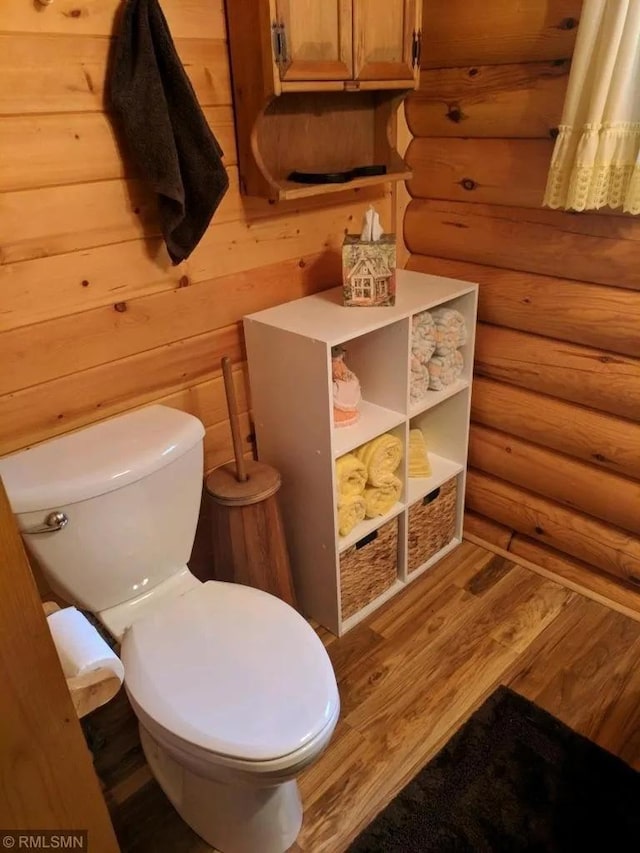 half bath with rustic walls, wood finished floors, and toilet
