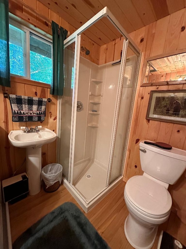 bathroom featuring toilet, wood walls, wood finished floors, and a stall shower