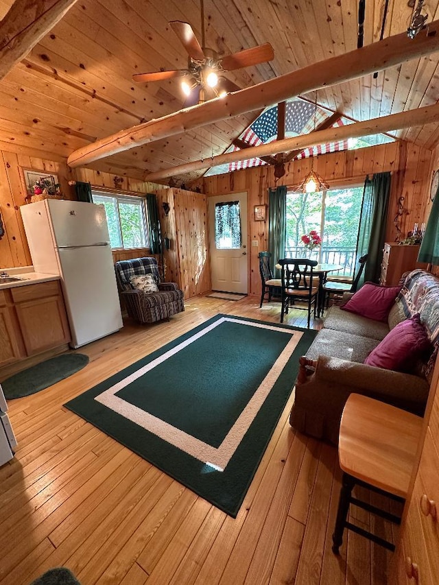 interior space with wood walls, light wood-style flooring, a ceiling fan, and lofted ceiling with beams