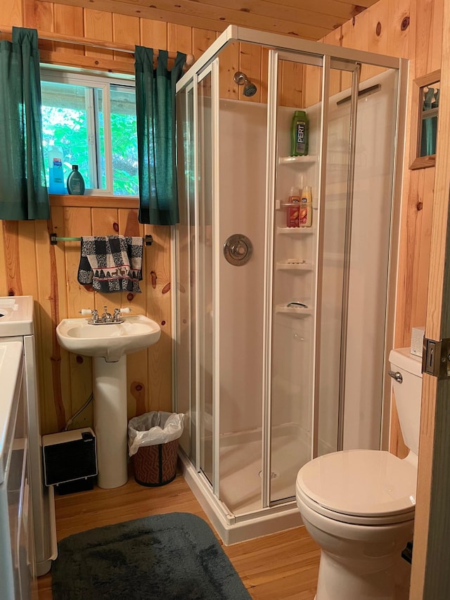 bathroom featuring toilet, wood walls, a shower stall, and wood finished floors