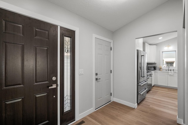 entrance foyer featuring vaulted ceiling, light wood-style floors, and baseboards