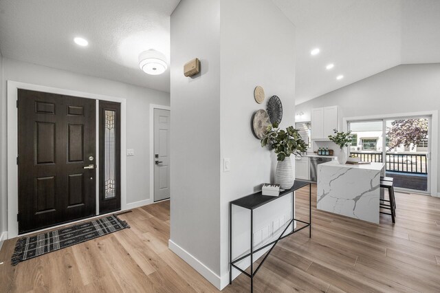 foyer entrance with light wood-type flooring, baseboards, recessed lighting, and high vaulted ceiling