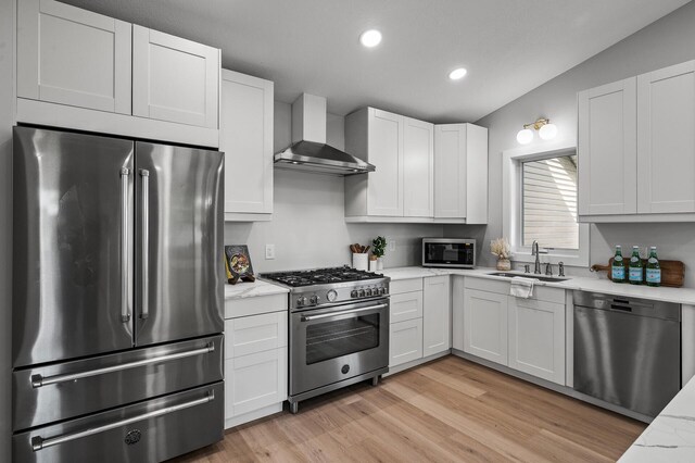kitchen featuring appliances with stainless steel finishes, wall chimney range hood, a sink, recessed lighting, and light wood-type flooring