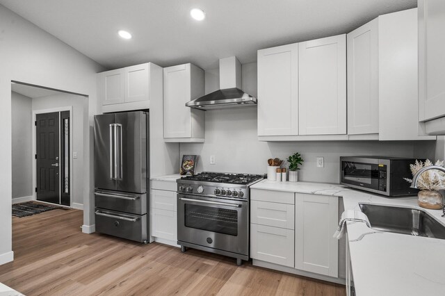 kitchen featuring high end appliances, wall chimney range hood, light wood-style floors, recessed lighting, and a sink