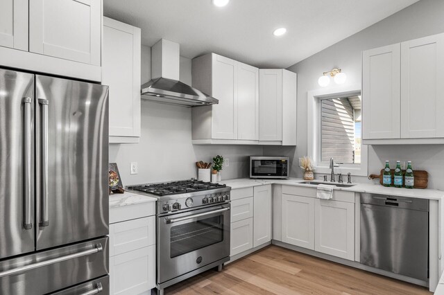 kitchen featuring premium appliances, wall chimney range hood, a sink, light wood-style floors, and recessed lighting