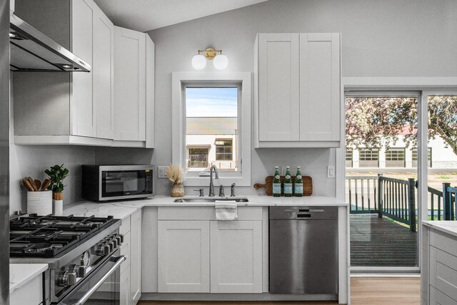 kitchen featuring stainless steel appliances, a sink, exhaust hood, and white cabinets