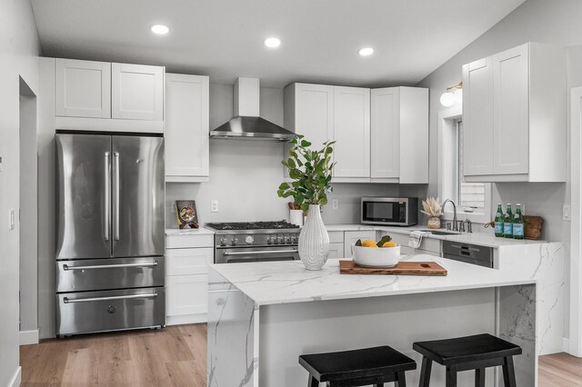 kitchen featuring stainless steel appliances, wall chimney range hood, a sink, a breakfast bar, and recessed lighting
