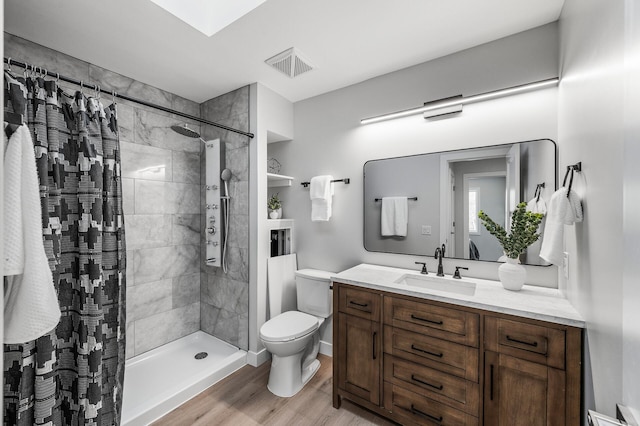 bathroom with tiled shower, toilet, wood finished floors, and vanity