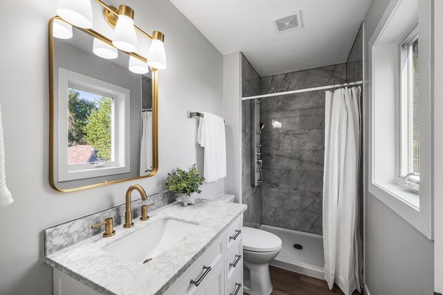 bathroom featuring vanity, wood finished floors, a stall shower, toilet, and a textured ceiling