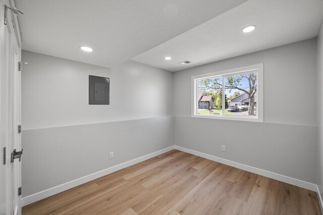 basement with electric panel, light wood-style flooring, baseboards, and recessed lighting