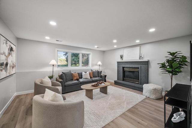 living area with light wood-style flooring, a brick fireplace, recessed lighting, and baseboards