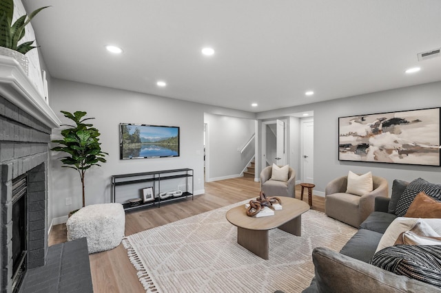 living area featuring a brick fireplace, stairway, light wood-type flooring, baseboards, and recessed lighting
