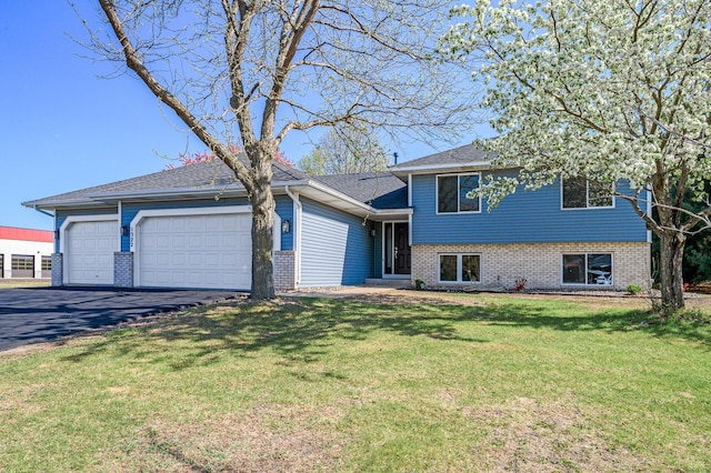 split level home featuring an attached garage, asphalt driveway, brick siding, and a front lawn