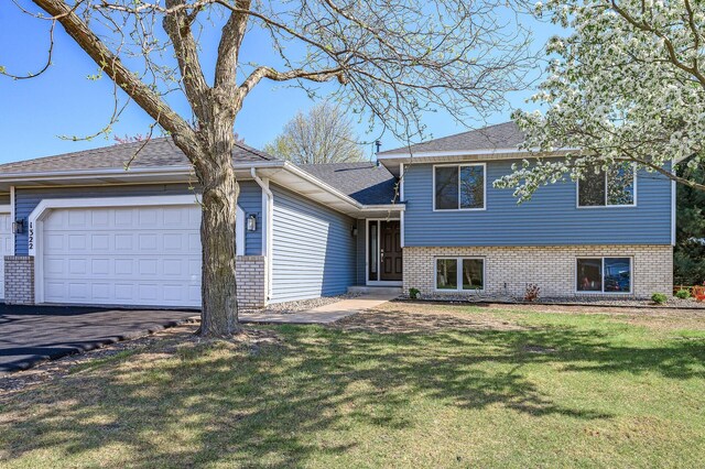 split level home featuring an attached garage, brick siding, a front lawn, driveway, and a shingled roof