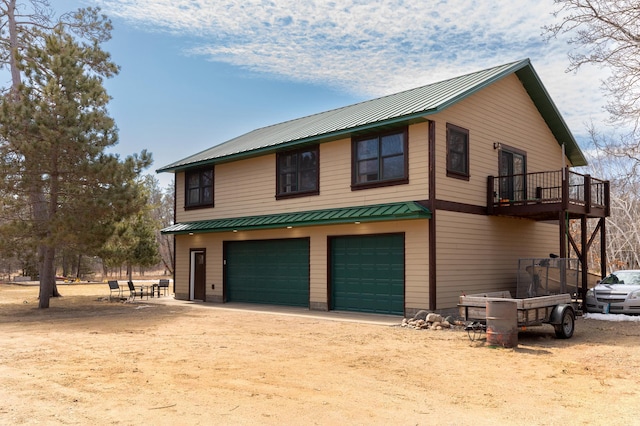 view of side of home featuring a balcony, a standing seam roof, dirt driveway, metal roof, and a garage