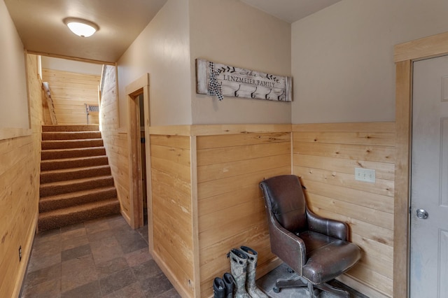 hallway featuring wooden walls, stone finish flooring, and stairs