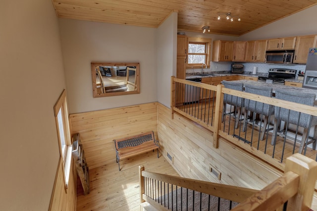kitchen featuring a sink, stainless steel appliances, light wood finished floors, decorative backsplash, and wood ceiling