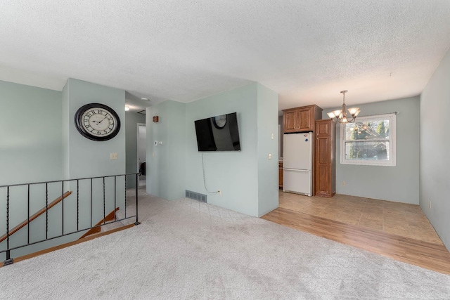 unfurnished living room featuring light colored carpet, a chandelier, and a textured ceiling