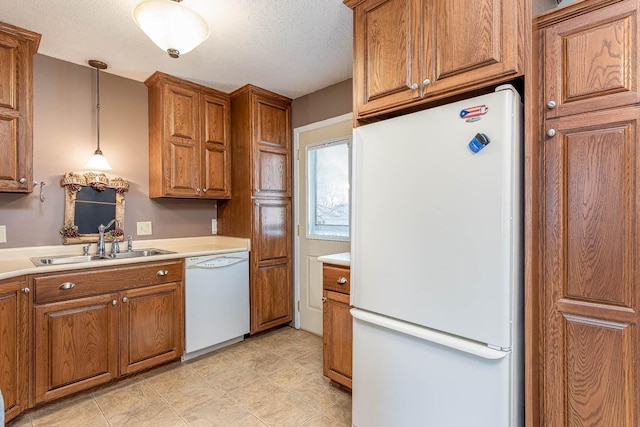 kitchen featuring white appliances, brown cabinetry, a sink, and a textured ceiling