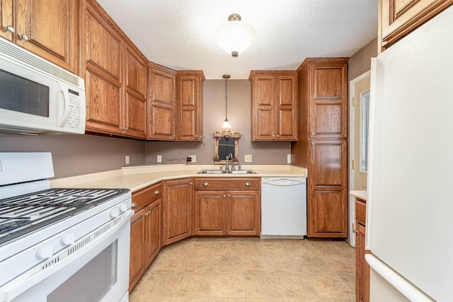kitchen with white appliances, a sink, brown cabinetry, and a textured ceiling