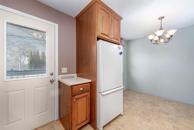 kitchen with freestanding refrigerator, a chandelier, brown cabinetry, light countertops, and a textured ceiling