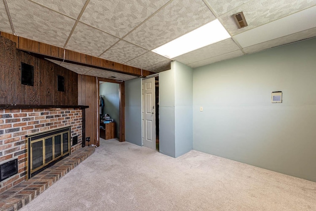 unfurnished living room with carpet, a brick fireplace, a drop ceiling, and wooden walls