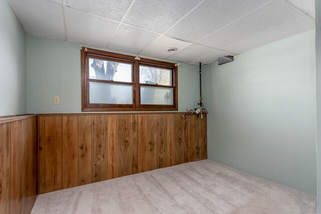 carpeted empty room featuring wood walls, a paneled ceiling, and wainscoting