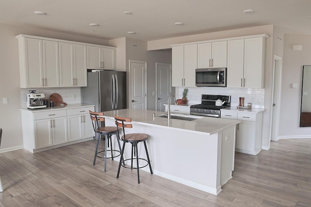5275 94th Ln N, Brooklyn Park, MN 55443 - kitchen featuring light wood finished floors, a sink, backsplash, stainless steel appliances, and an island with sink