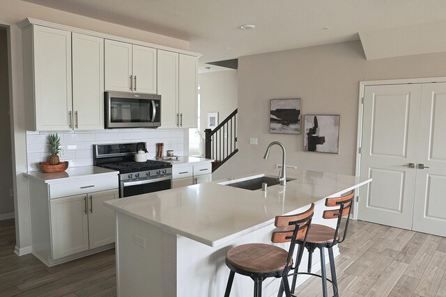 5275 94th Ln N, Brooklyn Park, MN 55443 - kitchen with a sink, a kitchen island with sink, light wood-type flooring, backsplash, and appliances with stainless steel finishes