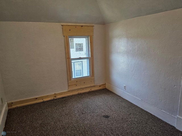 carpeted empty room featuring vaulted ceiling, a textured wall, and baseboards