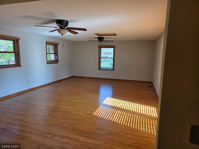 empty room featuring a textured ceiling, baseboards, a ceiling fan, and wood finished floors
