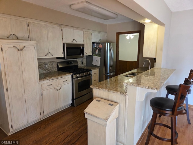 kitchen with light stone counters, a sink, a peninsula, appliances with stainless steel finishes, and dark wood-style floors