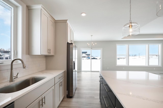 kitchen with light wood-style floors, stainless steel refrigerator with ice dispenser, tasteful backsplash, a sink, and decorative light fixtures