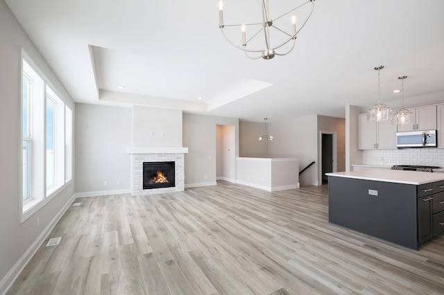 kitchen featuring baseboards, light wood-type flooring, light countertops, stainless steel microwave, and backsplash