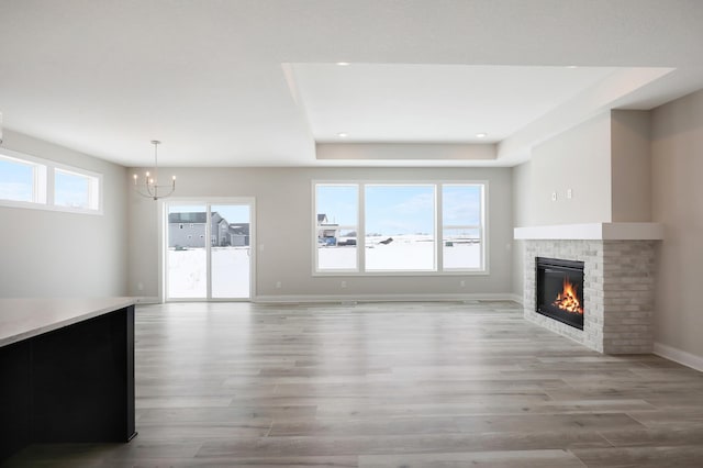 unfurnished living room with a brick fireplace, an inviting chandelier, light wood-style flooring, and a raised ceiling