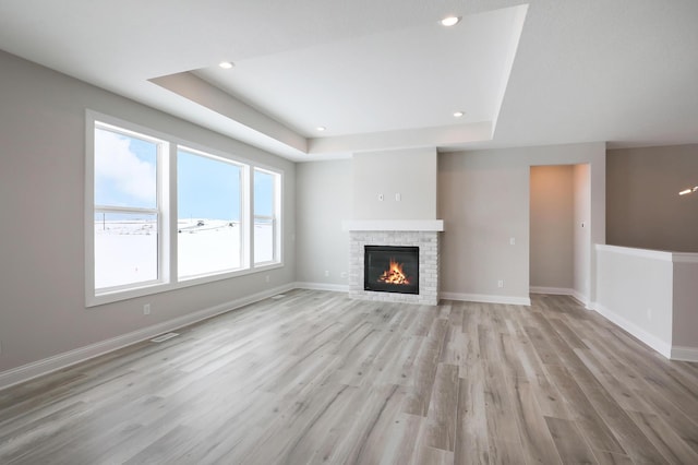 unfurnished living room featuring a tray ceiling, a glass covered fireplace, baseboards, and light wood finished floors