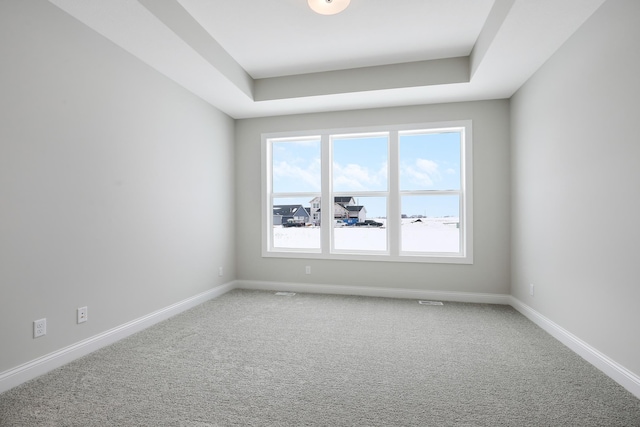 carpeted spare room featuring baseboards and a tray ceiling